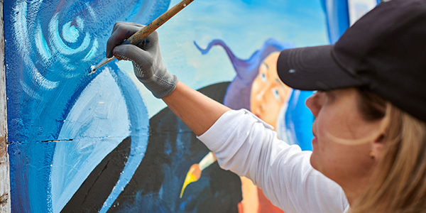 Photo of a woman painting a mural on the side of a building.