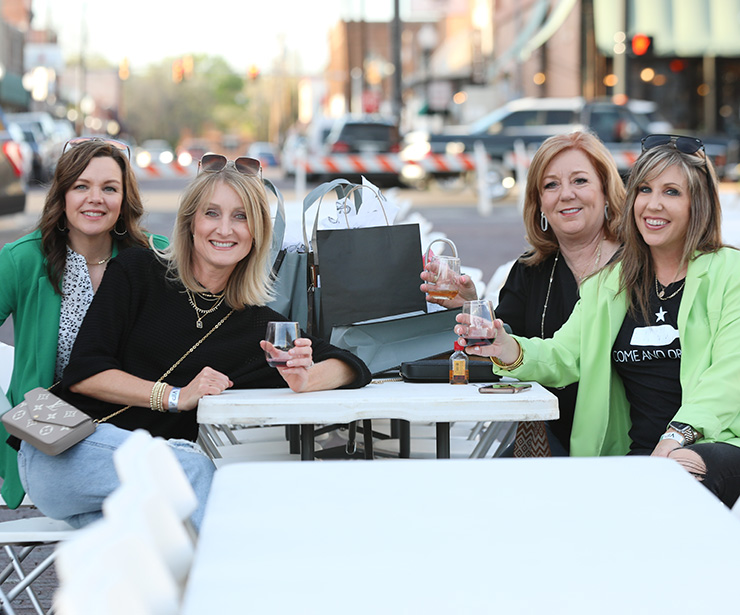 shopping-header-img-desktop Photo of a group of women sitting at an outdoor table posing with their shopping haul.